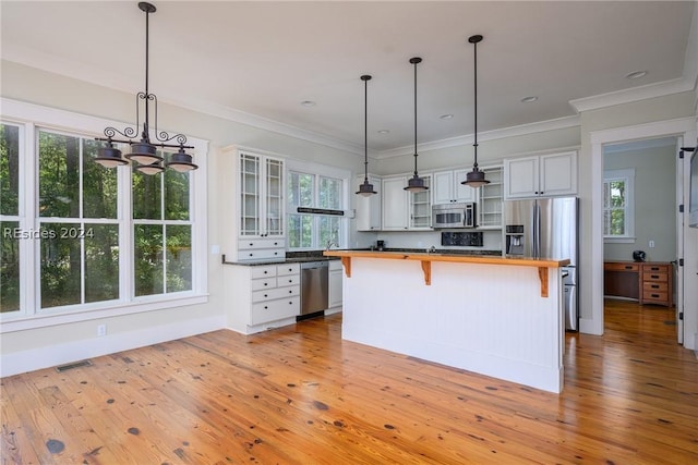 kitchen with pendant lighting, stainless steel appliances, a kitchen island, and white cabinets