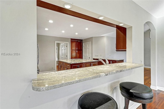 kitchen featuring a kitchen island, dark wood-type flooring, light stone counters, and kitchen peninsula