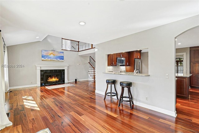 living room with dark wood-type flooring, vaulted ceiling, and a tile fireplace