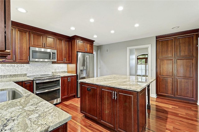 kitchen featuring appliances with stainless steel finishes, dark hardwood / wood-style floors, light stone countertops, a kitchen island, and decorative backsplash