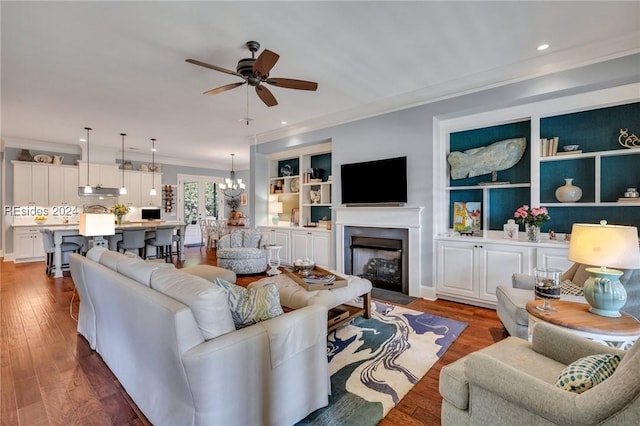 living room featuring ceiling fan with notable chandelier, ornamental molding, built in features, and dark hardwood / wood-style floors