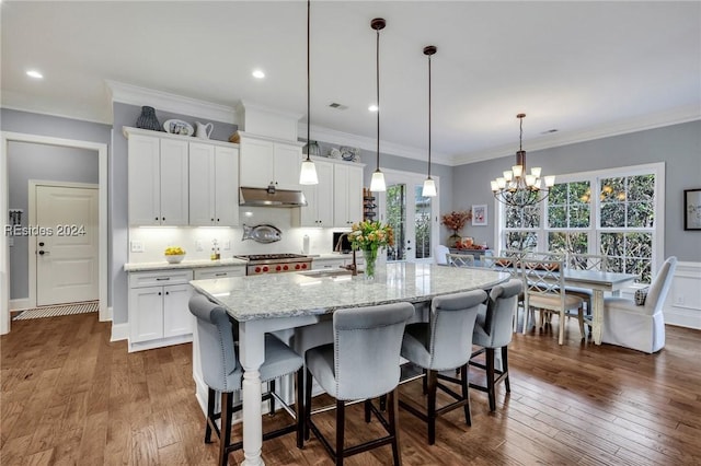 kitchen featuring white cabinetry, hanging light fixtures, a kitchen island with sink, dark hardwood / wood-style floors, and light stone counters