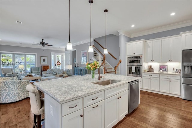 kitchen with appliances with stainless steel finishes, pendant lighting, white cabinetry, sink, and a kitchen island with sink