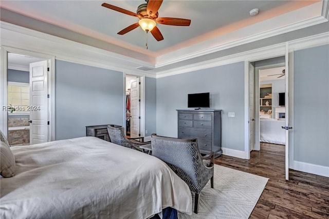 bedroom with ensuite bath, dark wood-type flooring, a raised ceiling, and ceiling fan