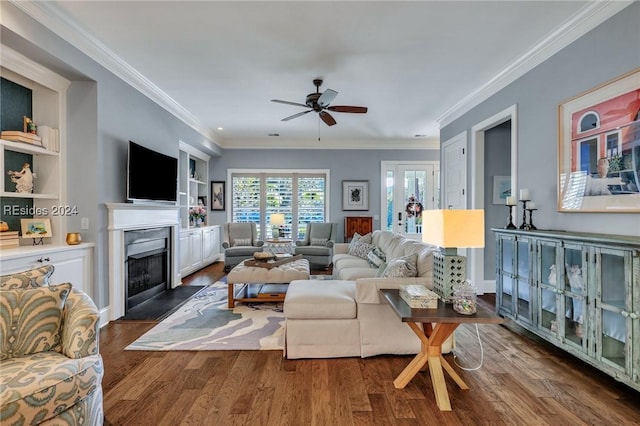 living room with ornamental molding, dark wood-type flooring, ceiling fan, and built in shelves