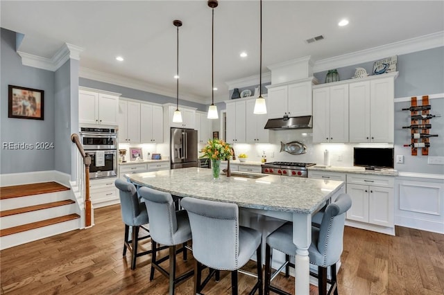 kitchen with white cabinetry, light stone counters, decorative light fixtures, appliances with stainless steel finishes, and an island with sink