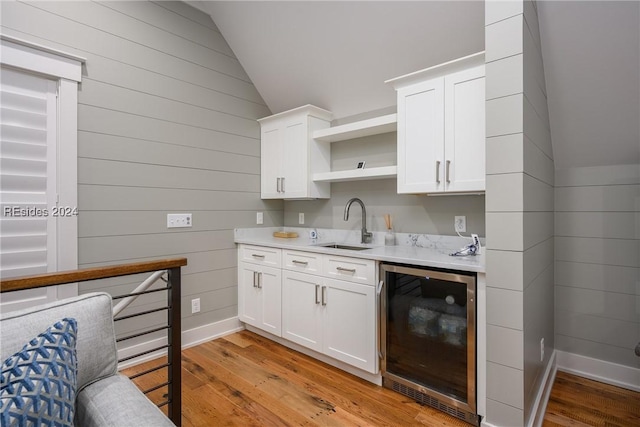 kitchen featuring sink, light hardwood / wood-style floors, white cabinets, vaulted ceiling, and beverage cooler