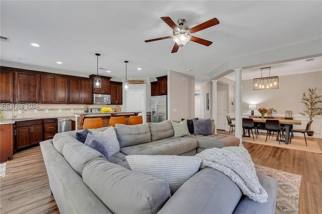 living room with sink, light hardwood / wood-style flooring, ceiling fan, and ornate columns