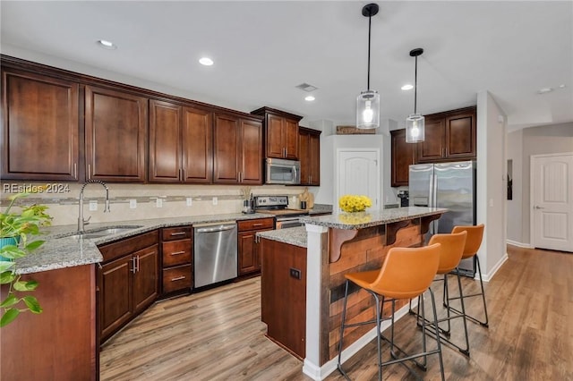 kitchen featuring sink, light stone counters, hanging light fixtures, a kitchen island, and stainless steel appliances