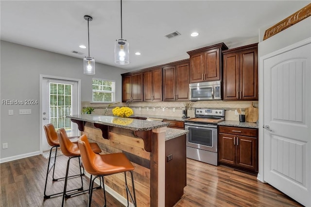 kitchen featuring a breakfast bar, light stone counters, decorative light fixtures, a center island, and appliances with stainless steel finishes