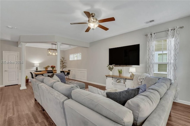 living room with ornate columns, wood-type flooring, and ceiling fan with notable chandelier