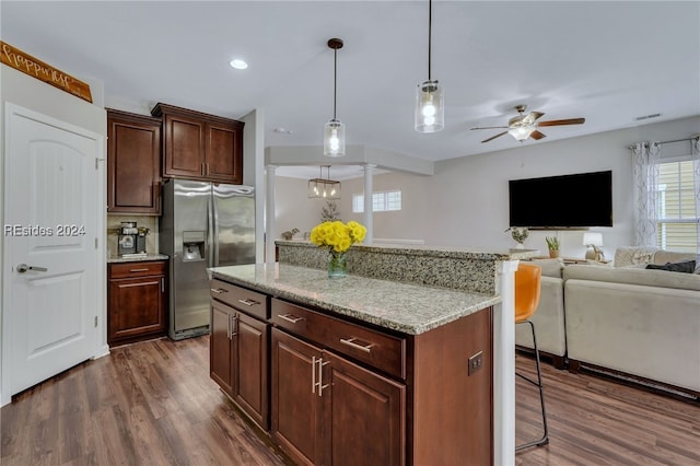 kitchen featuring decorative light fixtures, dark wood-type flooring, light stone counters, stainless steel refrigerator with ice dispenser, and dark brown cabinets