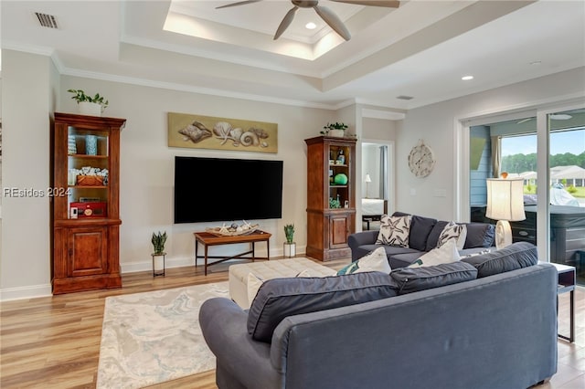 living room featuring crown molding, a tray ceiling, ceiling fan, and light wood-type flooring