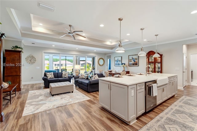 kitchen featuring an island with sink, a tray ceiling, dishwasher, and decorative light fixtures