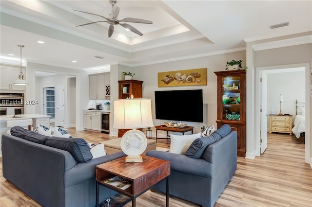 living room featuring crown molding, beverage cooler, a raised ceiling, and light hardwood / wood-style flooring