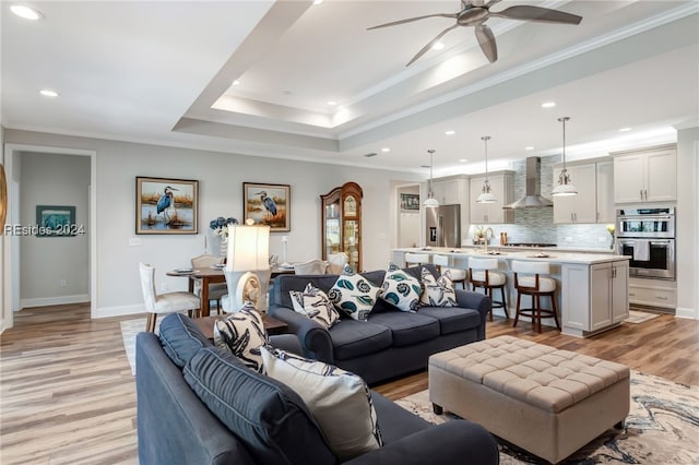 living room featuring sink, crown molding, light hardwood / wood-style flooring, ceiling fan, and a tray ceiling