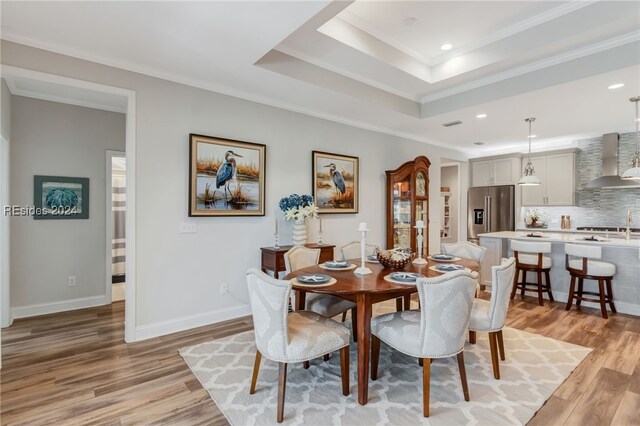 dining room with crown molding, light hardwood / wood-style floors, and a tray ceiling