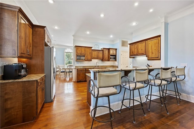 kitchen featuring light stone counters, stainless steel appliances, dark hardwood / wood-style flooring, and a breakfast bar area