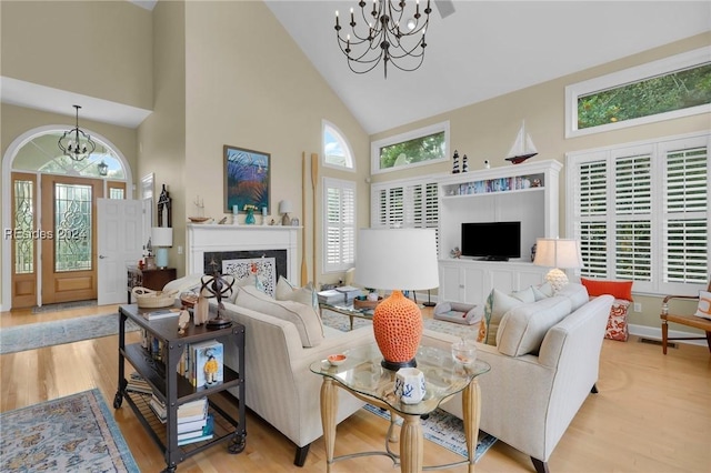 living room with a notable chandelier, light hardwood / wood-style flooring, high vaulted ceiling, and a premium fireplace