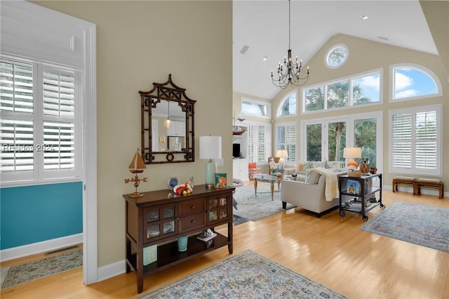 living room with a healthy amount of sunlight, high vaulted ceiling, a chandelier, and light wood-type flooring