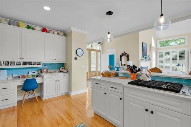 kitchen with hanging light fixtures, built in desk, white cabinets, and backsplash