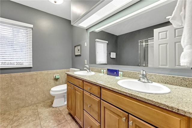 bathroom with a shower with shower door, tile walls, vanity, toilet, and tile patterned floors