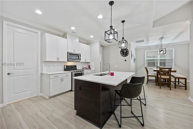 kitchen with sink, a center island with sink, appliances with stainless steel finishes, pendant lighting, and white cabinets