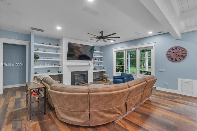 living room featuring ceiling fan, dark hardwood / wood-style floors, a fireplace, built in shelves, and beamed ceiling