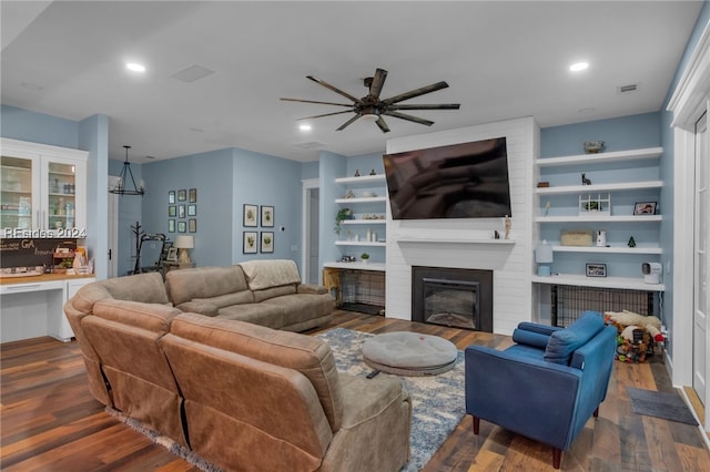 living room featuring built in features, dark wood-type flooring, and a large fireplace