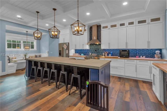 kitchen with pendant lighting, white cabinets, wall chimney exhaust hood, and a center island with sink