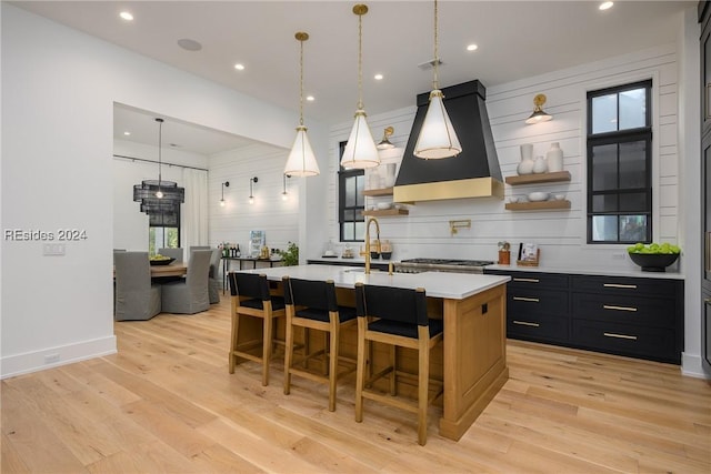 kitchen featuring a breakfast bar, island range hood, light hardwood / wood-style flooring, an island with sink, and pendant lighting