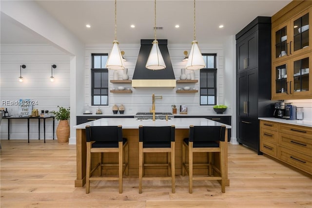 kitchen featuring island range hood, light wood-type flooring, decorative light fixtures, and a center island with sink