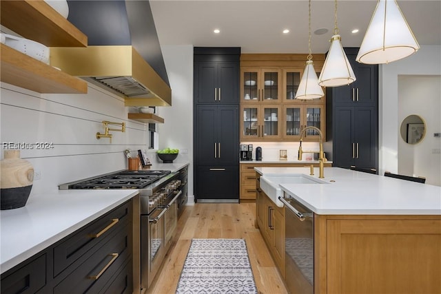 kitchen with island range hood, decorative light fixtures, sink, stainless steel appliances, and a center island with sink