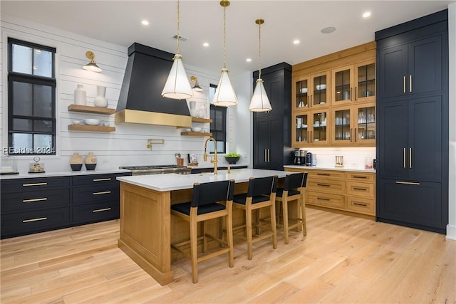 kitchen with a breakfast bar, a kitchen island with sink, decorative light fixtures, exhaust hood, and light wood-type flooring