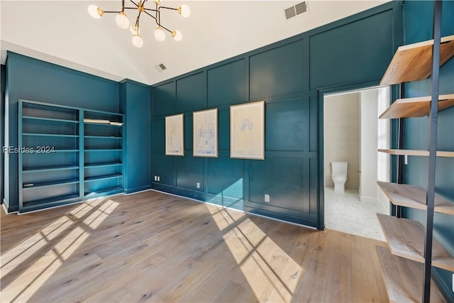 spare room featuring wood-type flooring, a chandelier, and vaulted ceiling