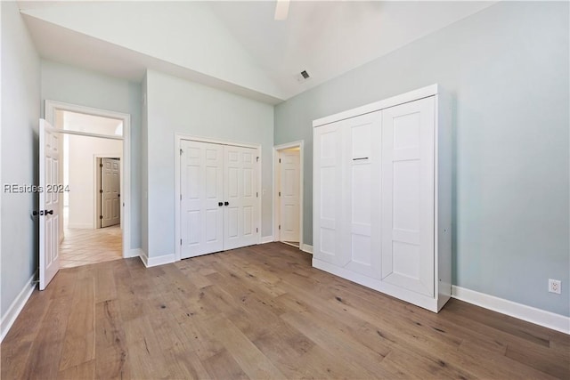 unfurnished bedroom featuring high vaulted ceiling, two closets, ceiling fan, and light hardwood / wood-style flooring