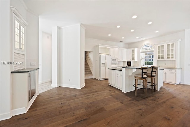 kitchen with white cabinetry, a kitchen bar, decorative backsplash, a center island, and dark wood-type flooring