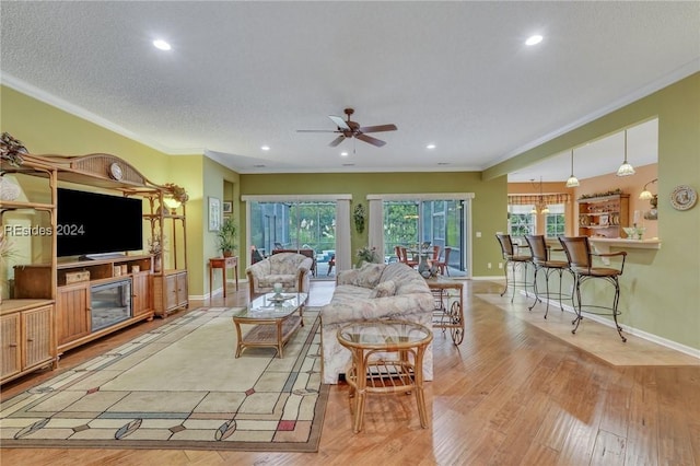 living room with a textured ceiling, ornamental molding, light hardwood / wood-style floors, and ceiling fan