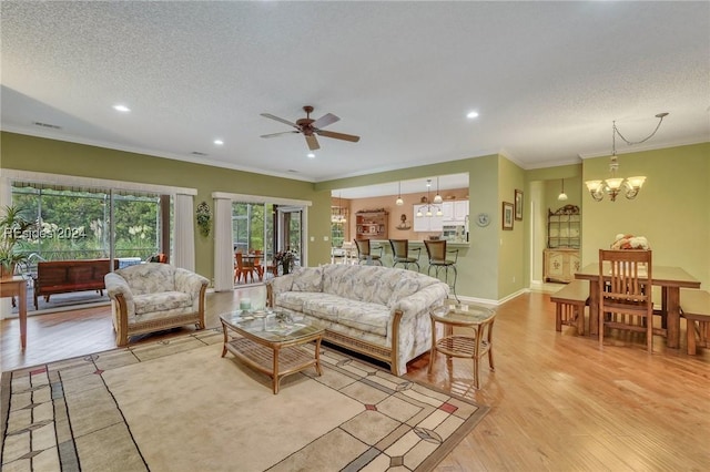 living room with ceiling fan with notable chandelier, ornamental molding, light hardwood / wood-style floors, and a textured ceiling