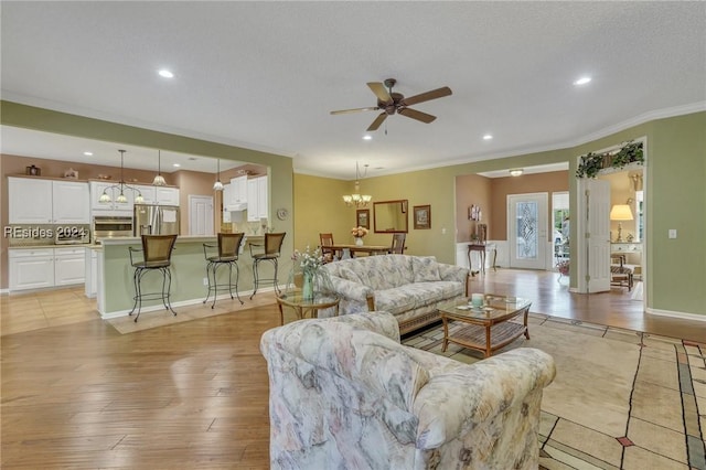 living room with crown molding, ceiling fan with notable chandelier, a textured ceiling, and light wood-type flooring