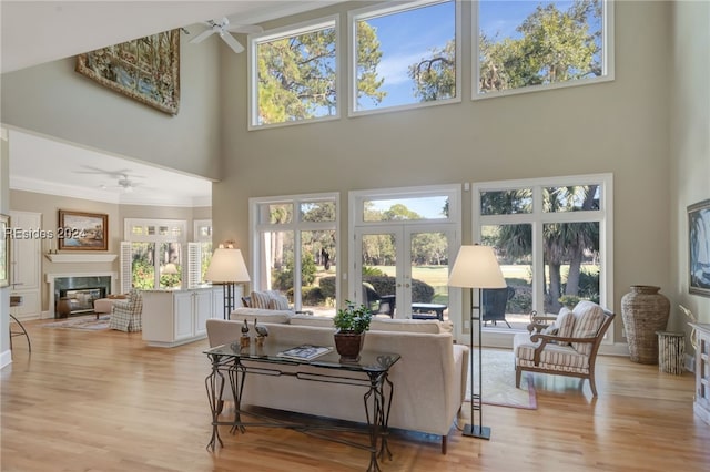 living room with ceiling fan, a wealth of natural light, light hardwood / wood-style flooring, and a high ceiling