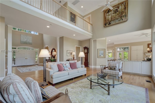 living room with ceiling fan, a towering ceiling, and light hardwood / wood-style floors