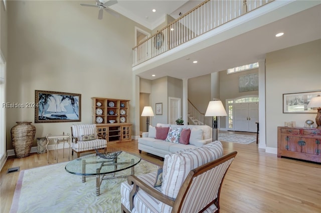 living room with a high ceiling, ornamental molding, ceiling fan, and light wood-type flooring