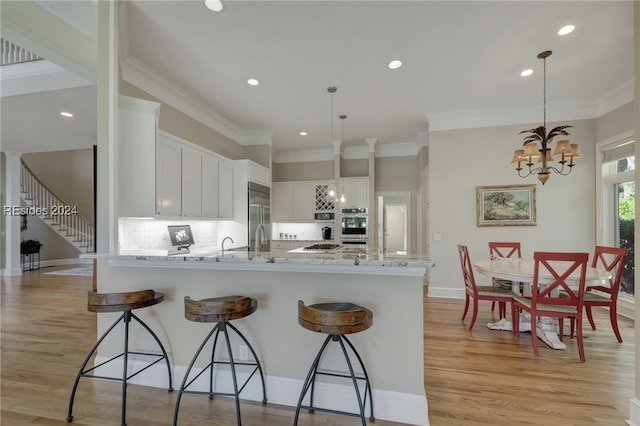 kitchen with light hardwood / wood-style flooring, white cabinetry, light stone counters, decorative backsplash, and decorative light fixtures