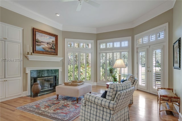 interior space with a fireplace, ceiling fan, light hardwood / wood-style floors, crown molding, and french doors