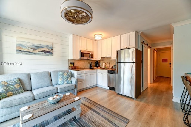 kitchen with white cabinetry, light hardwood / wood-style flooring, stainless steel appliances, a barn door, and backsplash