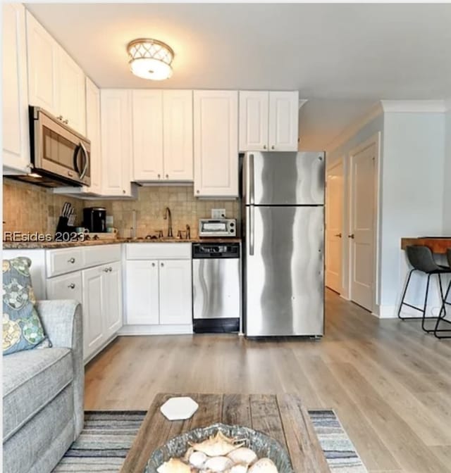 kitchen featuring sink, backsplash, stainless steel appliances, white cabinets, and light wood-type flooring