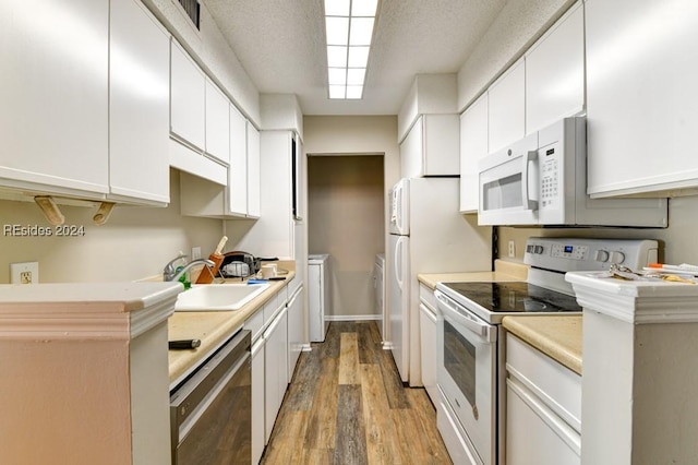 kitchen featuring sink, white cabinetry, separate washer and dryer, hardwood / wood-style flooring, and white appliances