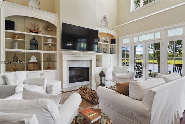 living room with a towering ceiling, built in features, a high end fireplace, and french doors