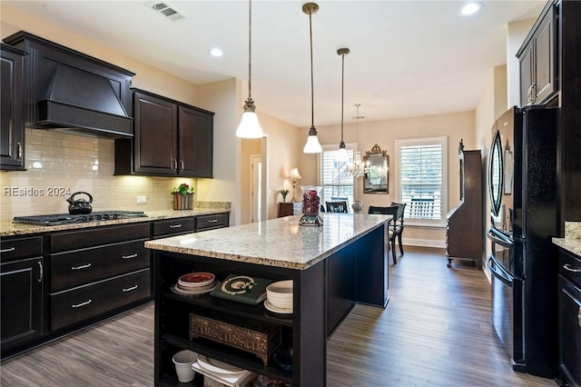 kitchen with pendant lighting, a center island, stainless steel gas cooktop, black fridge, and custom range hood